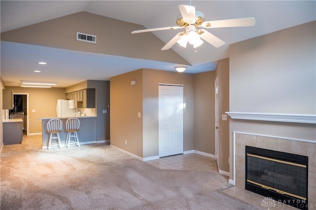 unfurnished living room with a tile fireplace, ceiling fan, light colored carpet, and lofted ceiling