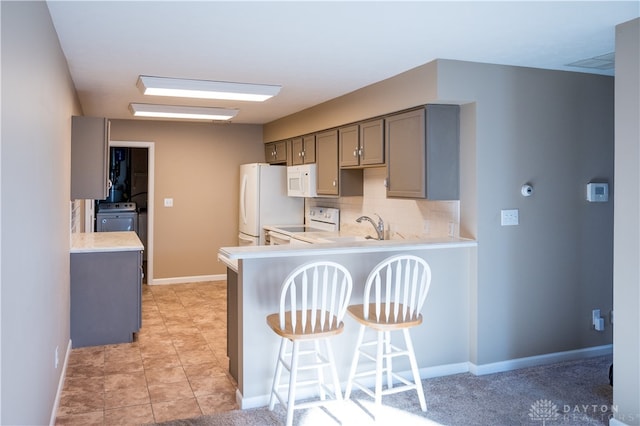 kitchen with white appliances, backsplash, gray cabinets, a kitchen bar, and kitchen peninsula