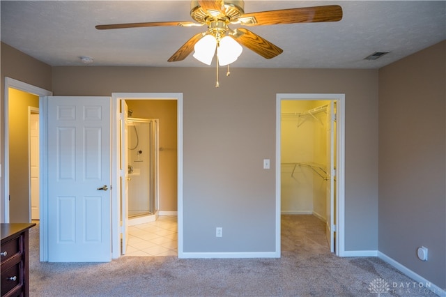 unfurnished bedroom with light carpet, a walk in closet, ceiling fan, a textured ceiling, and a closet