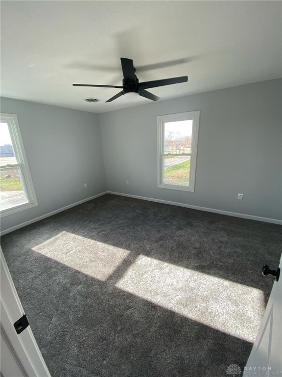 spare room with ceiling fan and dark colored carpet