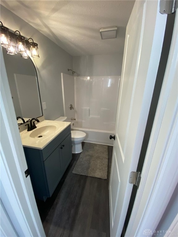 full bathroom with wood-type flooring, a textured ceiling, toilet, vanity, and bathtub / shower combination