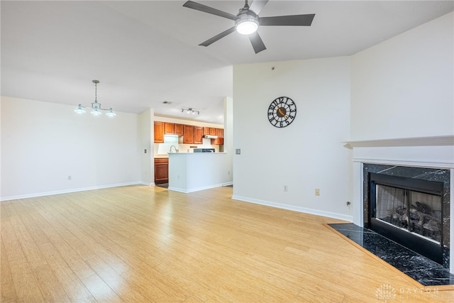 unfurnished living room with ceiling fan with notable chandelier, light hardwood / wood-style floors, and a high end fireplace