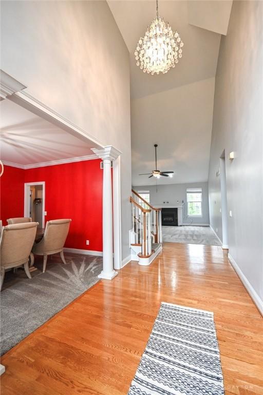 foyer featuring wood-type flooring, ceiling fan with notable chandelier, a high ceiling, and ornate columns