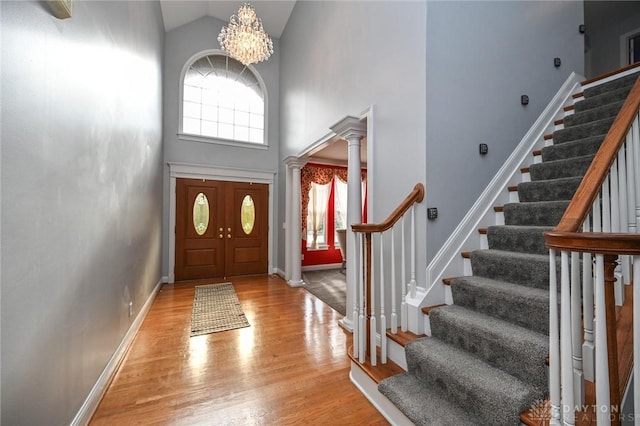 foyer featuring decorative columns, high vaulted ceiling, a chandelier, and light wood-type flooring