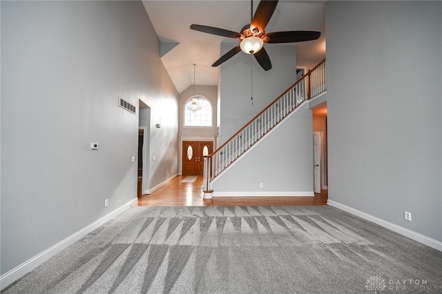 unfurnished living room featuring ceiling fan with notable chandelier, light colored carpet, and high vaulted ceiling