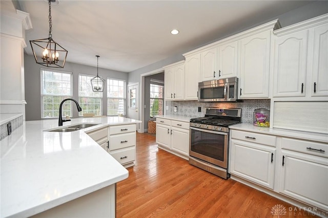 kitchen with sink, white cabinetry, hanging light fixtures, light wood-type flooring, and appliances with stainless steel finishes