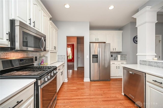 kitchen featuring ornate columns, white cabinetry, stainless steel appliances, light hardwood / wood-style floors, and decorative backsplash