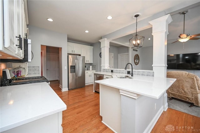 kitchen featuring sink, decorative columns, stainless steel appliances, white cabinets, and kitchen peninsula