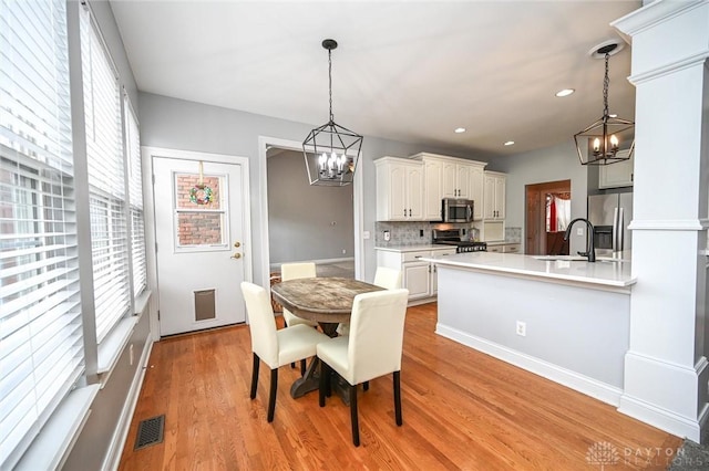 dining area with a notable chandelier, light hardwood / wood-style floors, sink, and ornate columns