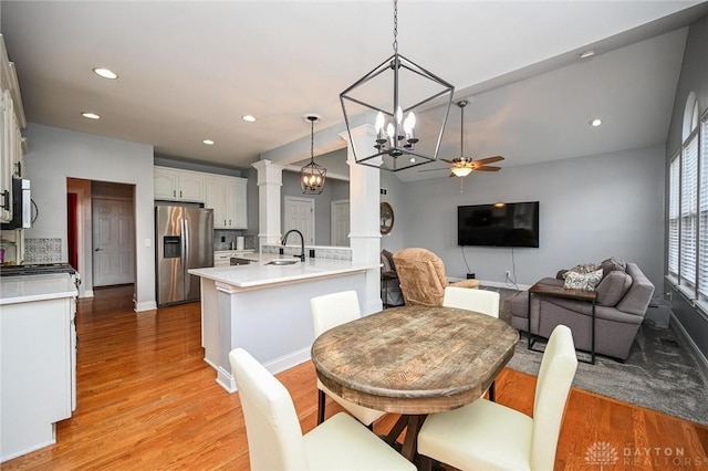 dining room with ceiling fan with notable chandelier, sink, light hardwood / wood-style flooring, and ornate columns