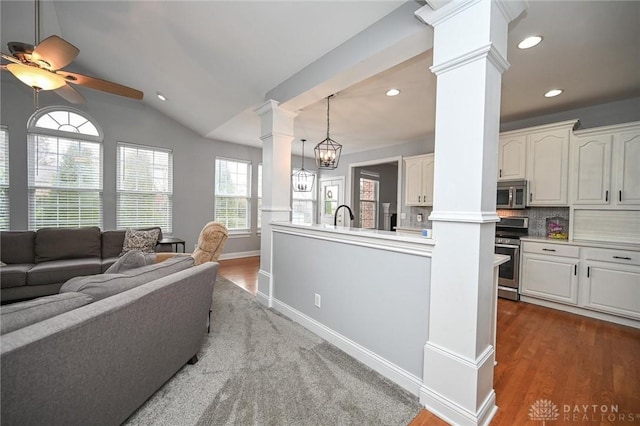 living room featuring ceiling fan with notable chandelier, decorative columns, lofted ceiling, sink, and light wood-type flooring