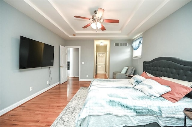 bedroom featuring ceiling fan, ensuite bath, a raised ceiling, and hardwood / wood-style floors