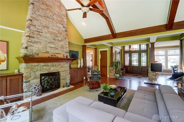 living room with light wood-type flooring, decorative columns, beam ceiling, high vaulted ceiling, and a stone fireplace