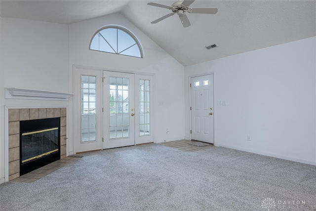 unfurnished living room with a tile fireplace, ceiling fan, high vaulted ceiling, and light colored carpet