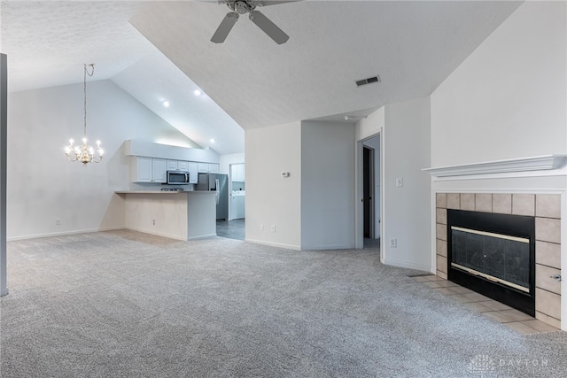 unfurnished living room with ceiling fan with notable chandelier, light carpet, a tile fireplace, and vaulted ceiling