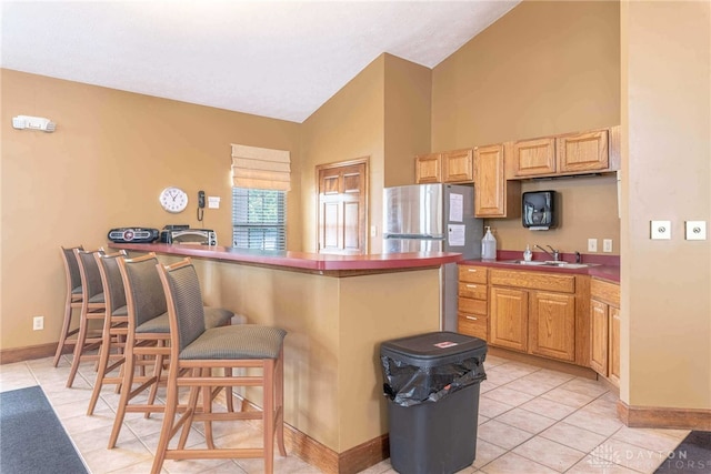 kitchen featuring sink, vaulted ceiling, kitchen peninsula, a breakfast bar area, and stainless steel refrigerator