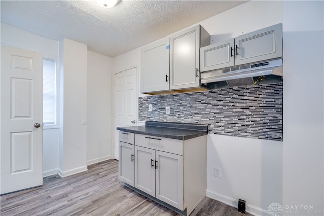 kitchen with a textured ceiling, gray cabinets, light hardwood / wood-style flooring, and backsplash