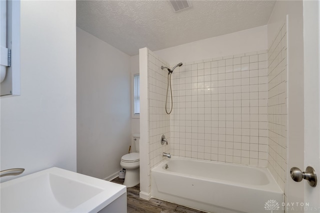 full bathroom with toilet, wood-type flooring, a textured ceiling, and tiled shower / bath