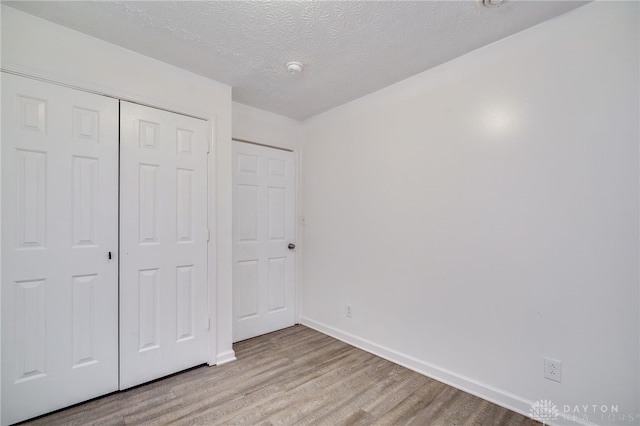 unfurnished bedroom featuring a textured ceiling, light hardwood / wood-style flooring, and a closet