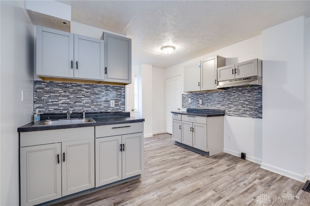 kitchen featuring decorative backsplash, light hardwood / wood-style floors, sink, and a textured ceiling