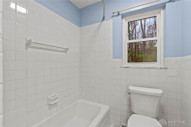 bathroom with a tub to relax in, a healthy amount of sunlight, toilet, and tile walls