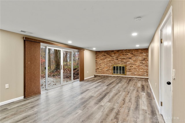 unfurnished living room with a fireplace, light wood-type flooring, and brick wall