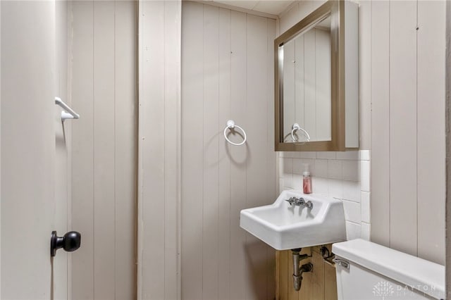 bathroom featuring toilet, wooden walls, and sink