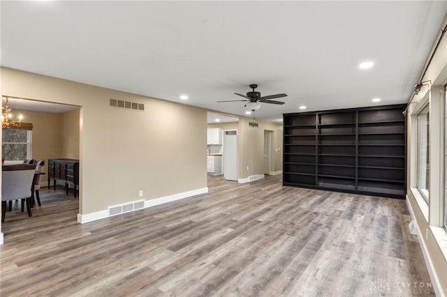 living room with hardwood / wood-style flooring, ceiling fan with notable chandelier, and built in shelves