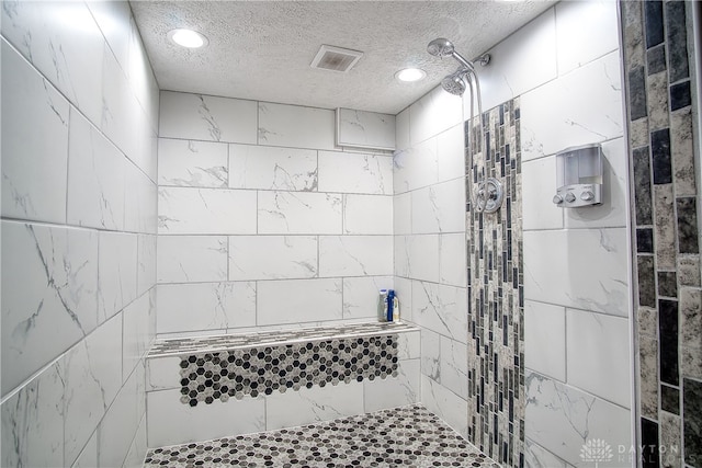 bathroom with a textured ceiling and tiled shower