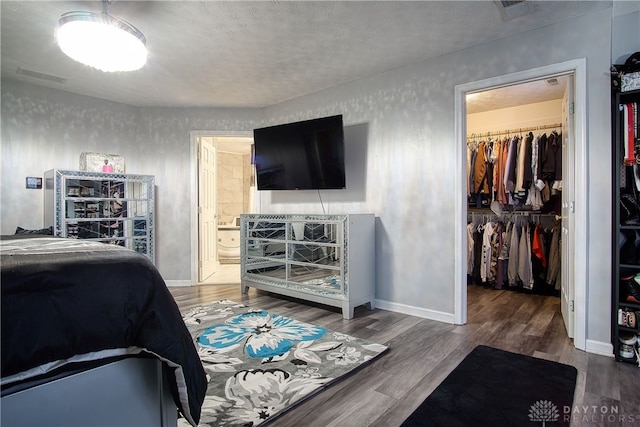 bedroom featuring a walk in closet, a closet, wood-type flooring, and a textured ceiling