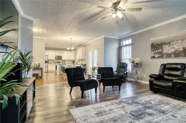 living room with a textured ceiling, ceiling fan with notable chandelier, crown molding, and light hardwood / wood-style flooring