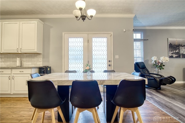 dining area featuring light hardwood / wood-style flooring, a chandelier, a textured ceiling, and ornamental molding