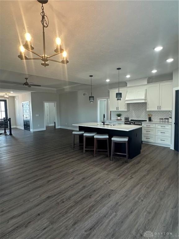 kitchen featuring white cabinetry, open floor plan, light countertops, an island with sink, and pendant lighting