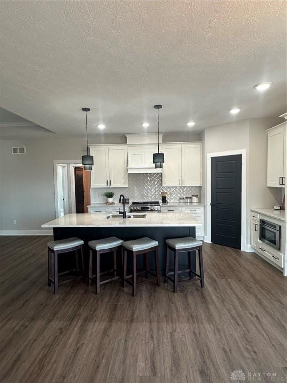 kitchen with light countertops, an island with sink, a sink, and white cabinetry