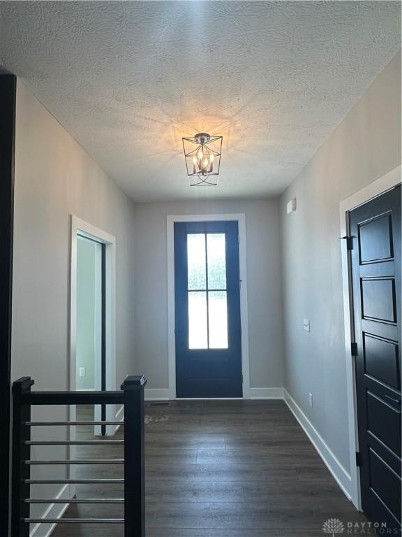 entrance foyer featuring a textured ceiling, baseboards, a chandelier, and dark wood-type flooring