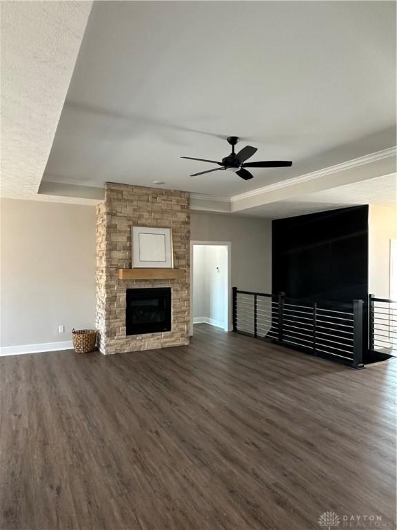 unfurnished living room featuring dark wood-style floors, a fireplace, a raised ceiling, ornamental molding, and baseboards