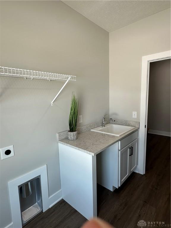 laundry area featuring a textured ceiling, a sink, cabinet space, dark wood finished floors, and electric dryer hookup