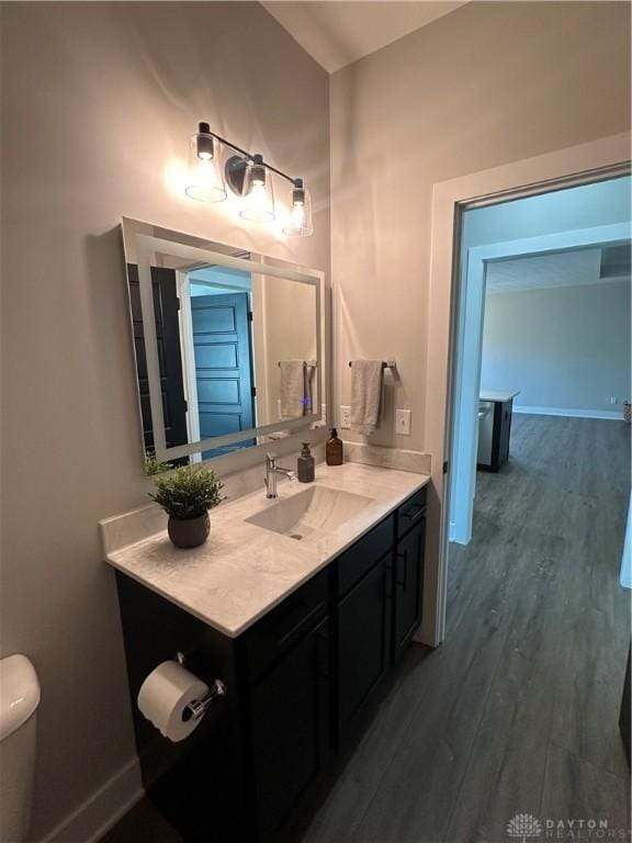 half bathroom featuring wood finished floors, vanity, and baseboards