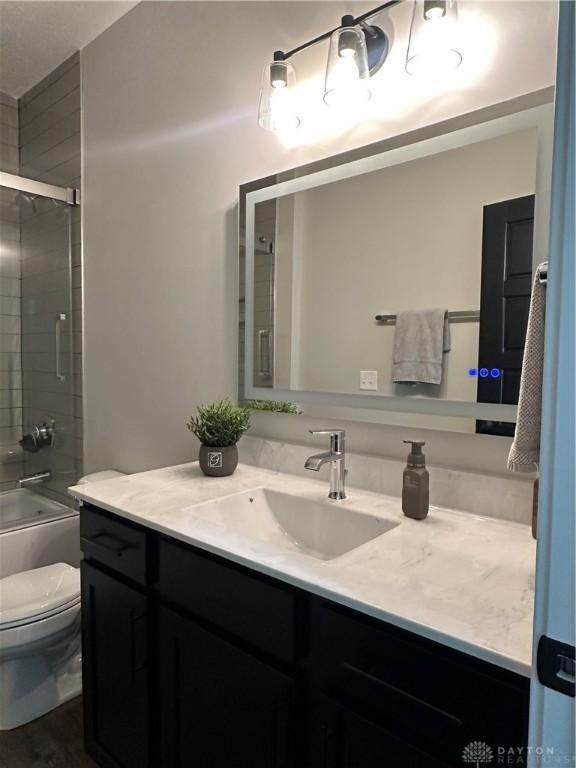 bathroom featuring toilet, bath / shower combo with glass door, and vanity