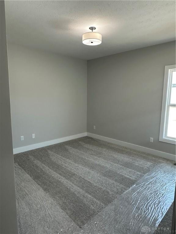 carpeted empty room with a textured ceiling and baseboards