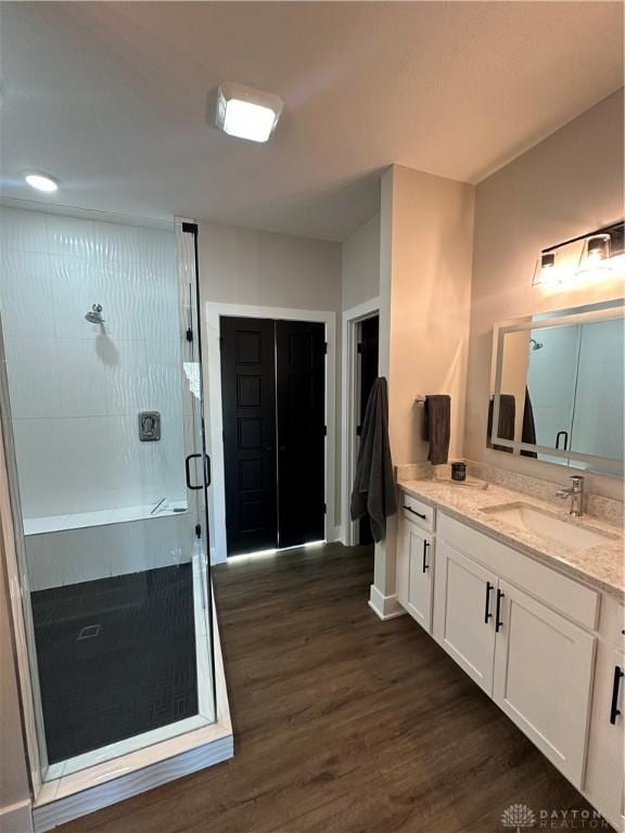 bathroom featuring wood finished floors, a shower stall, vanity, and baseboards