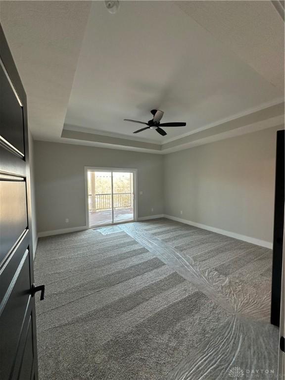 carpeted empty room with ceiling fan, baseboards, and a raised ceiling