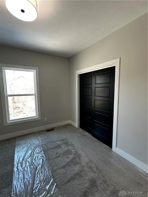 unfurnished bedroom with carpet flooring, a textured ceiling, and baseboards