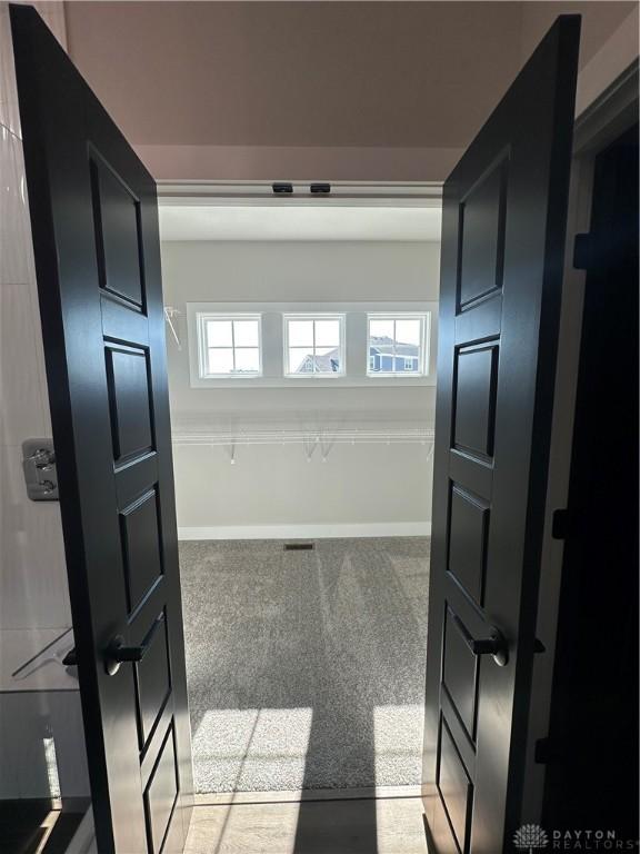 hallway with baseboards, plenty of natural light, and light colored carpet