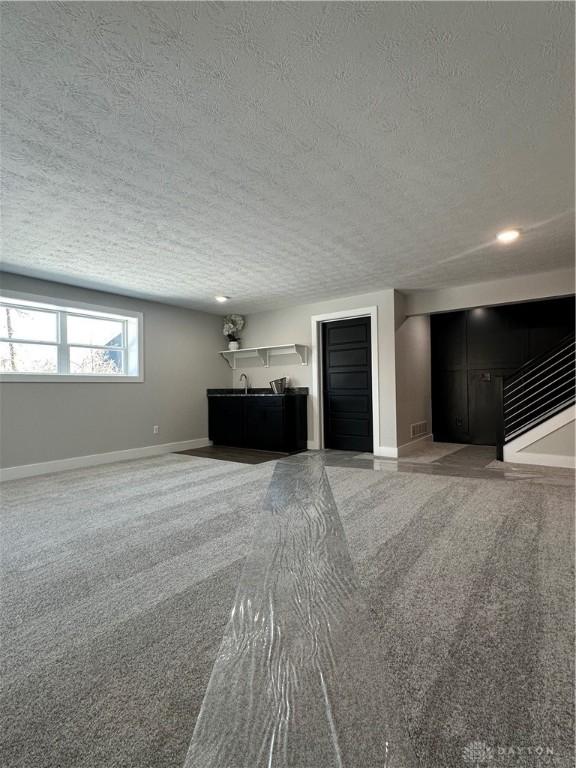 unfurnished living room with a textured ceiling, baseboards, and carpet flooring