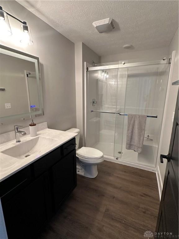 bathroom with toilet, wood finished floors, a textured ceiling, vanity, and a shower stall