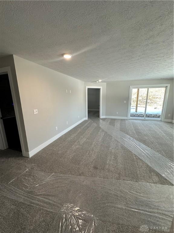 unfurnished room featuring dark colored carpet, a textured ceiling, and baseboards