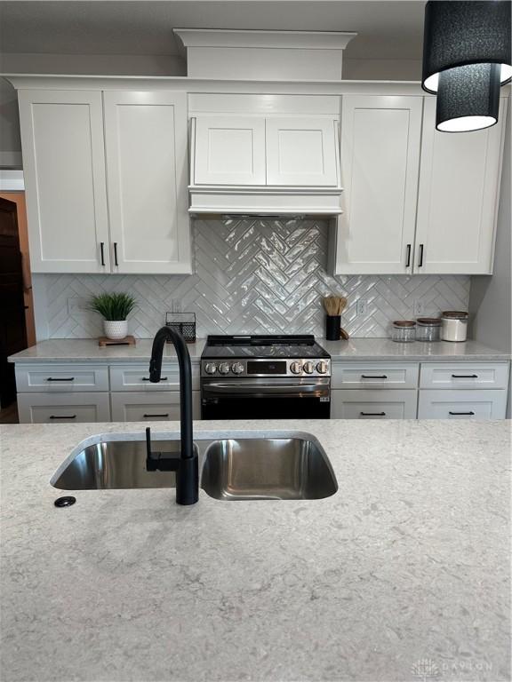 kitchen featuring a sink, white cabinetry, stainless steel range with electric cooktop, decorative backsplash, and custom range hood