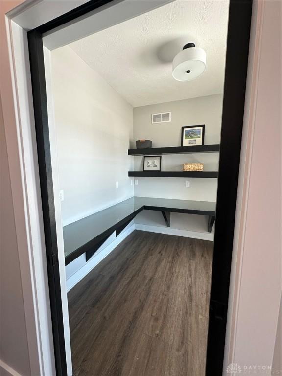 unfurnished office with dark wood-style floors, baseboards, visible vents, and a textured ceiling