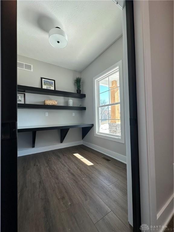 unfurnished office featuring dark wood-style flooring, visible vents, a textured ceiling, and baseboards